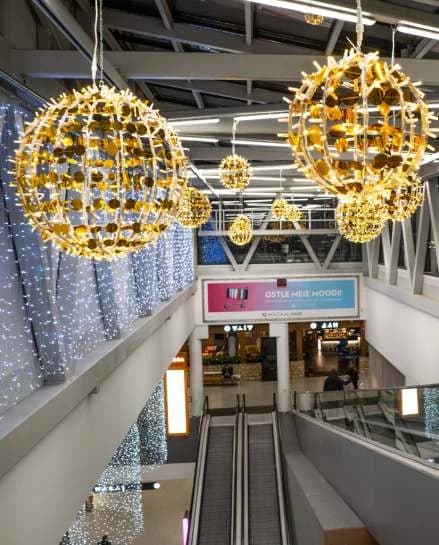 AVM galerisinde tavandan sarkan altın pullu ışık topları, yürüyen merdiven üstü