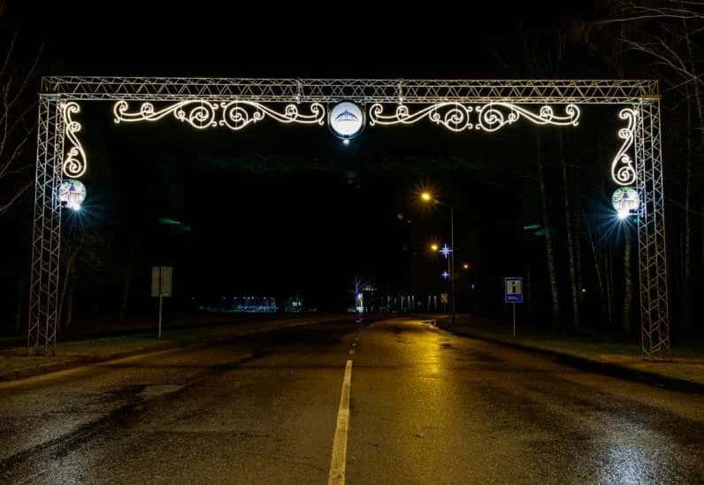 Ağaçlı bir yol girişinde LED tak kemeri, kemer ayaklarında dairesel madalyonlu sarmal direk süsleri