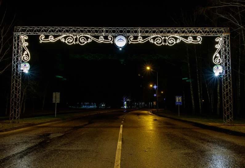Ağaçlı bir yol girişinde LED tak kemeri, kemer ayaklarında dairesel madalyonlu sarmal direk süsleri