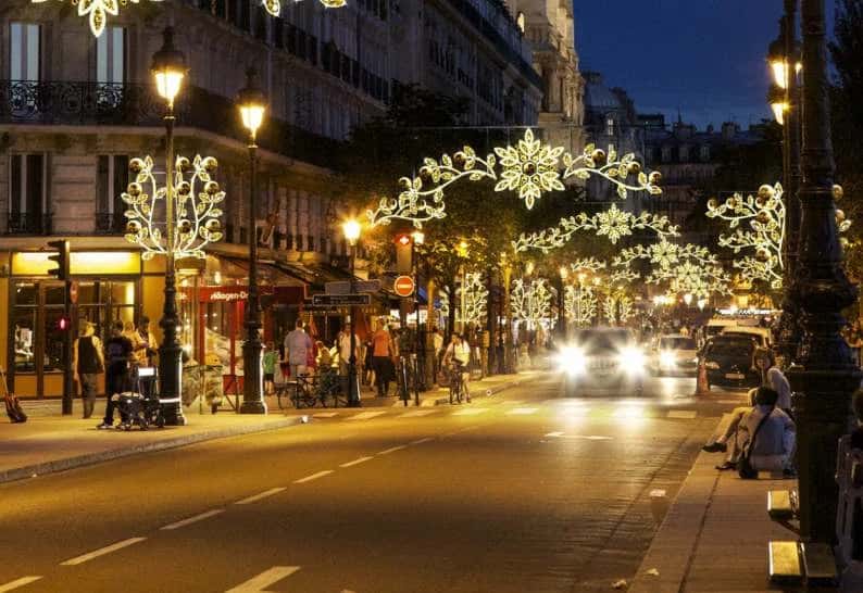 Paris caddesinde lamba direğine sarılmış yapraklı LED sarmaşık dalı, gece, arkada araç ışık izleri