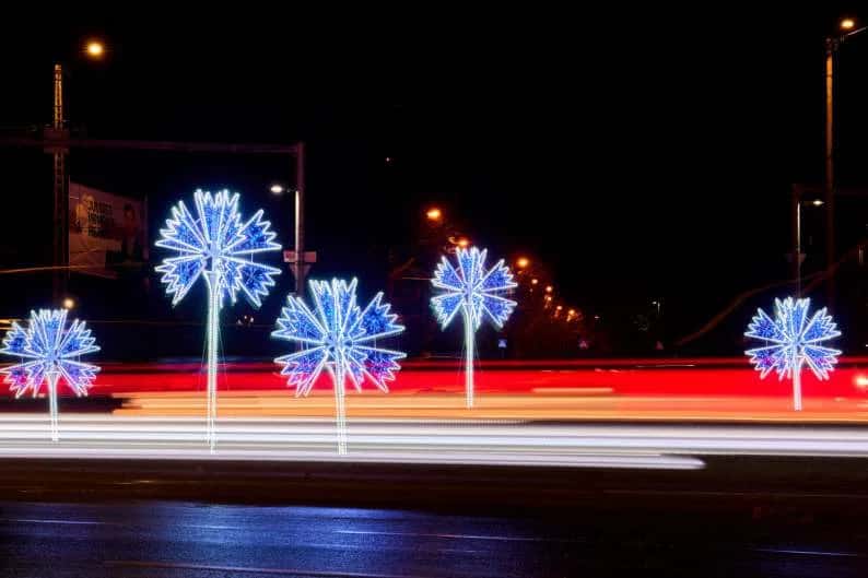 Cadde boyunca sıralı direk üstü mavi ışıklı patlamış yıldız motifleri, gece trafiği
