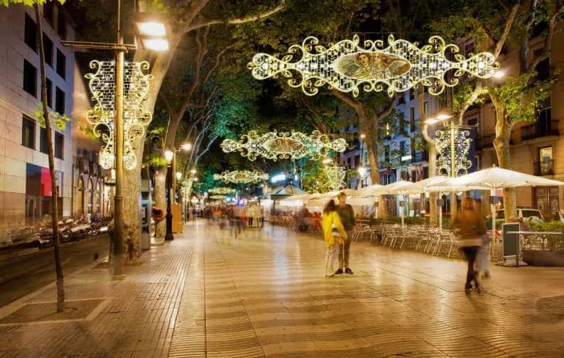 Ağaçlı yaya bulvarında ardışık asılı madalyonlu kristal sarkıtlar, gece kalabalığı altında