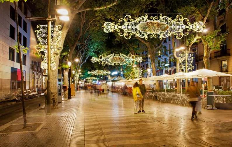 Ağaçlı yaya bulvarında ardışık asılı madalyonlu kristal sarkıtlar, gece kalabalığı altında